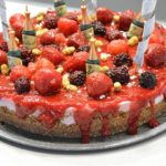 Close up of Vegan Strawberry Cheesecake dripping with strawberry cheesecake topping and decorated with strawberries and blackberries